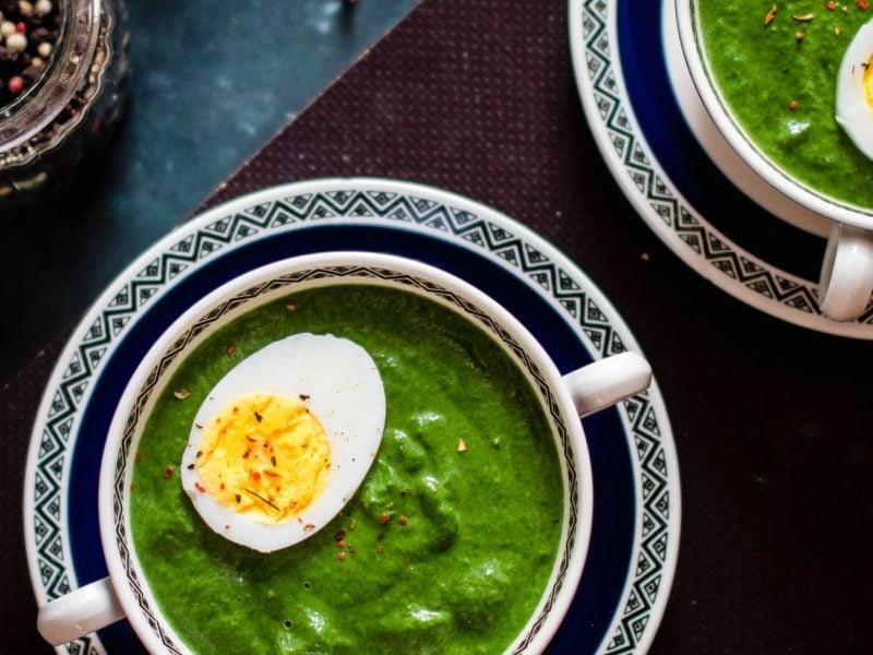 Zwei kleine Suppenschüsseln mit Grünkohl-Rahmsuppe mit einem halben Ei in der Draufsicht.