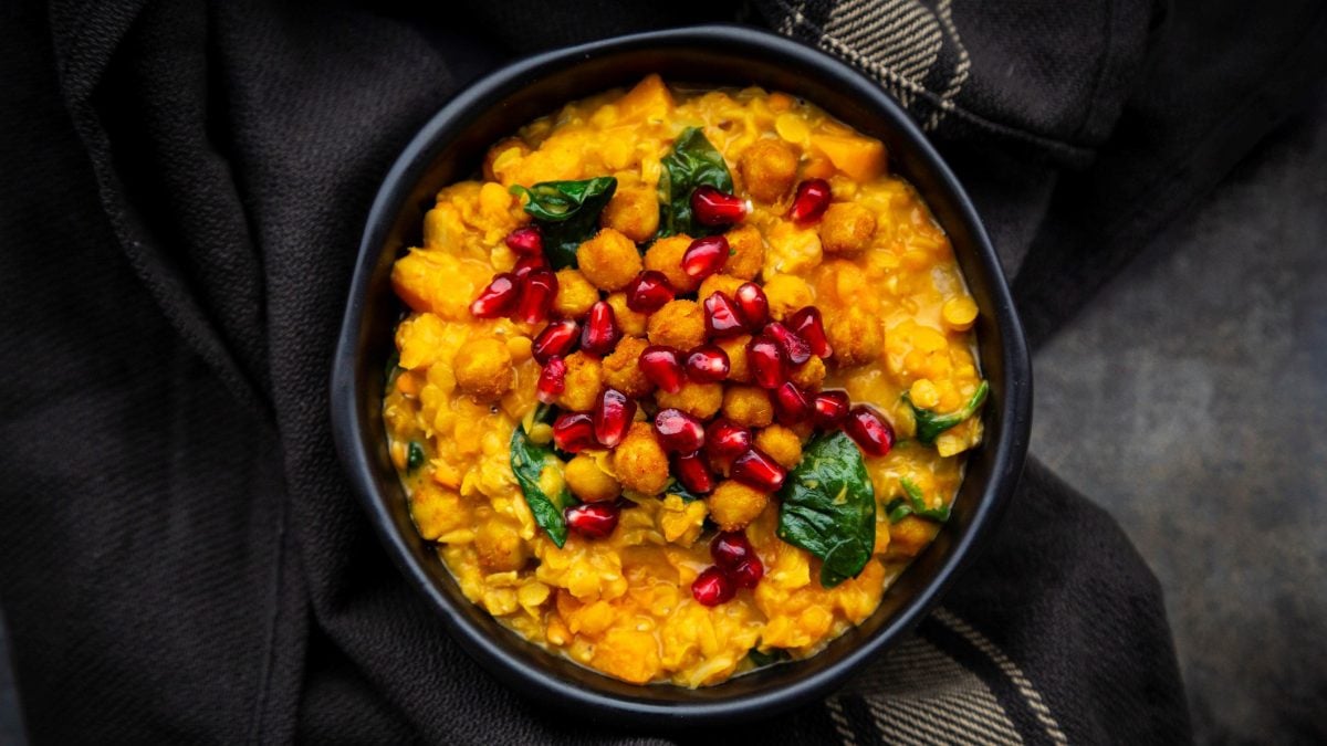 Ein dunkler Teller befüllt mit Kürbis-Linsencurry mit Spinat, Kichererbsen und Granatapfelkernen in der Draufsicht.