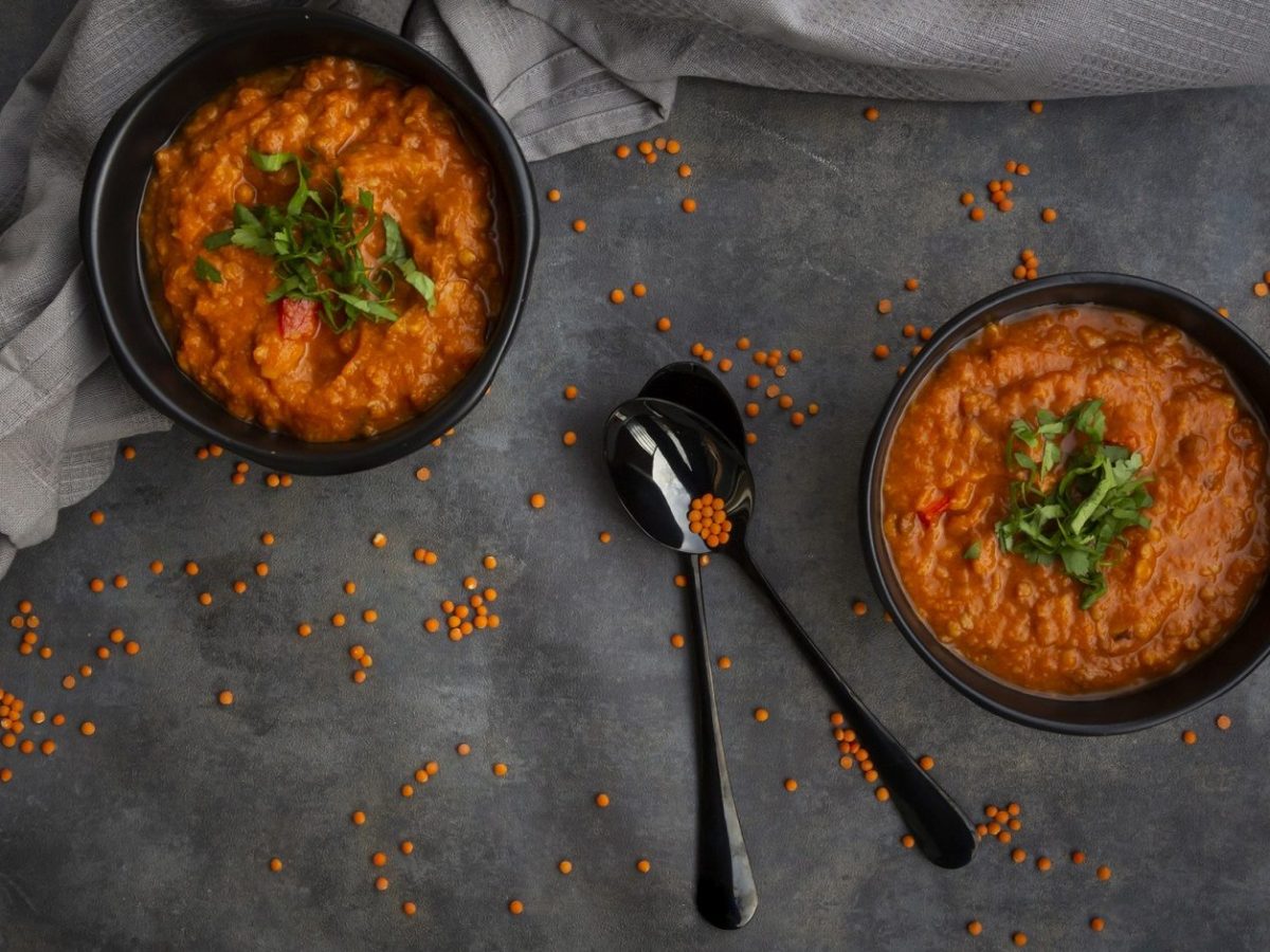 Zwei Schüsseln Rote Linsensuppe auf einem Tisch, dazu zwei Löffel und ein graues Geschirrtuch.