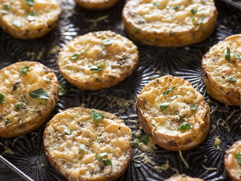 Ein Backblech mit Parmesan-Kartoffeln, die mit Kräutern bestreut sind.