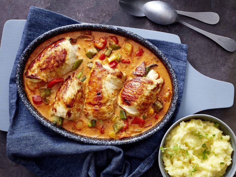 In einem großen Bräter sind Putenrouladen in Paprika-Sahne-Soße. Daneben steht eine Schale mit Kartoffelpüree.