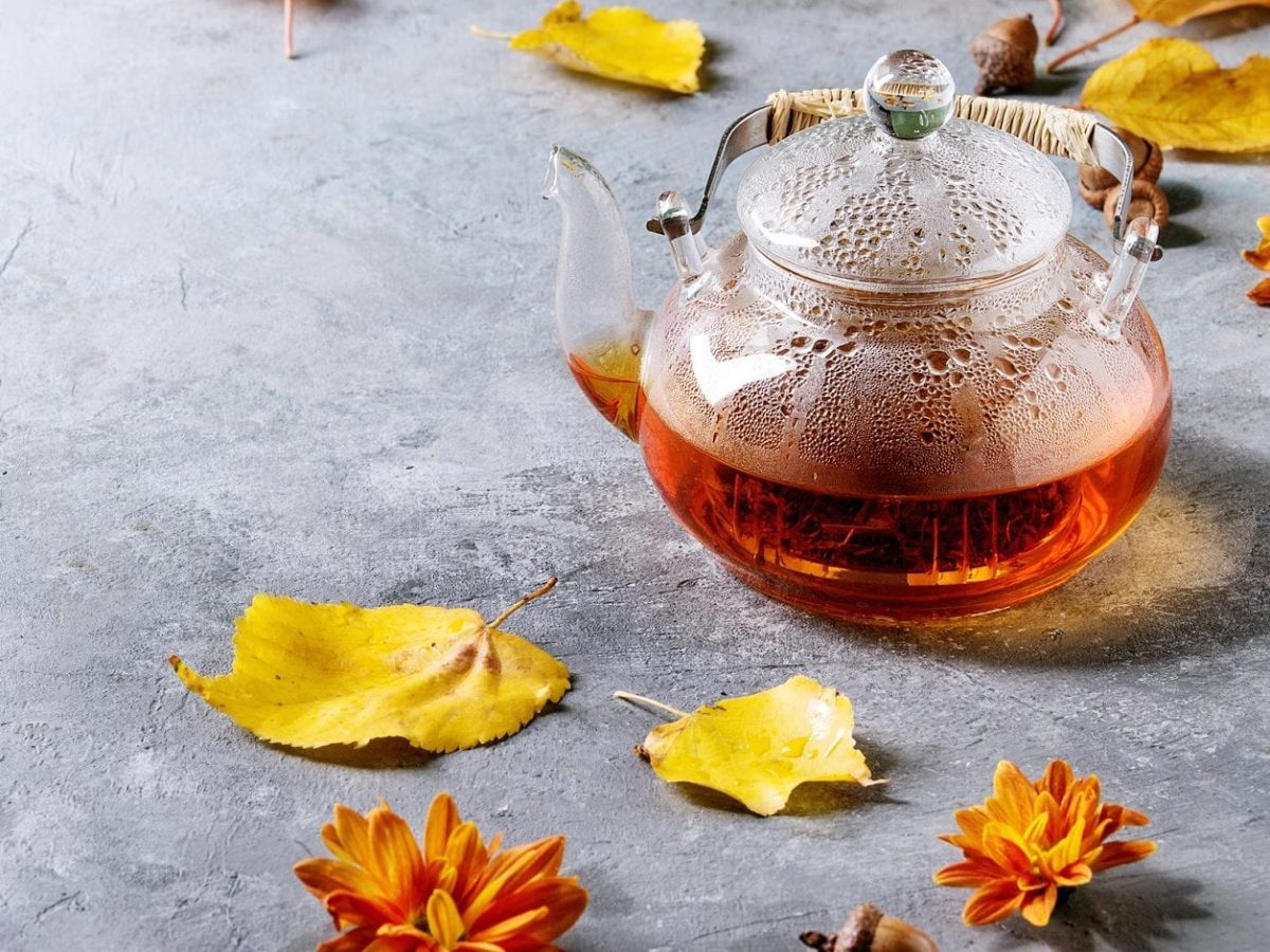 Da kommt heiße Herbststimmung auf: Unser Vanille-Kokos-Tee brüht in der Glas-Teekanne. Ringsum liegen bunte Blätter.