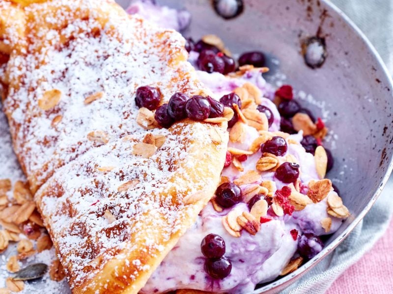 Blick von oben: Auf einem Teller liegt eine zusammen geklappte Waffel mit Heidelbeeren.