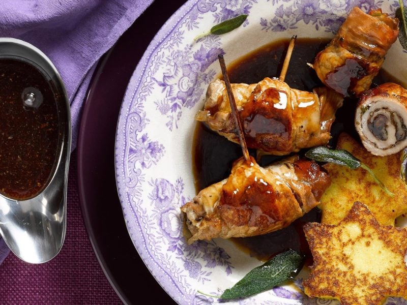 Die Balsamico-Rouladen mit Polenta-Sternen liegen mit etwas Salbei angerichtet auf einem tiefen Teller. Dazu gibt's Balsamico-Soße aus einer Sauciere.