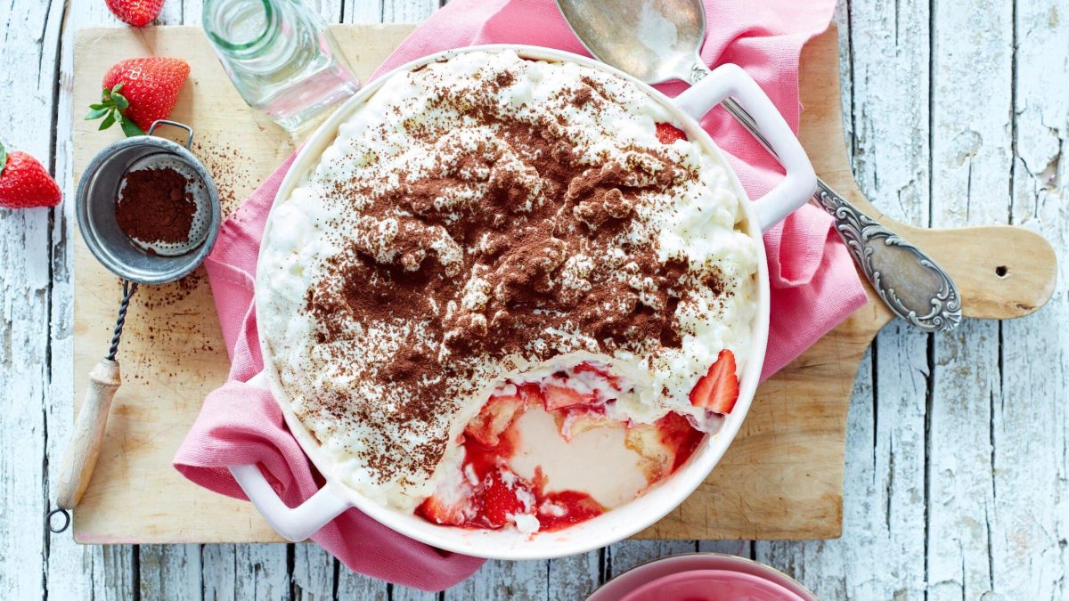 Unser Erdbeer-Milchreis-Tiramisu angerichtet in einer Henkel-Schüssel auf einem Holzbrett und mit pinker Serviette.