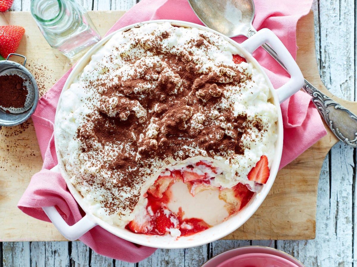 Unser Erdbeer-Milchreis-Tiramisu angerichtet in einer Henkel-Schüssel auf einem Holzbrett und mit pinker Serviette.