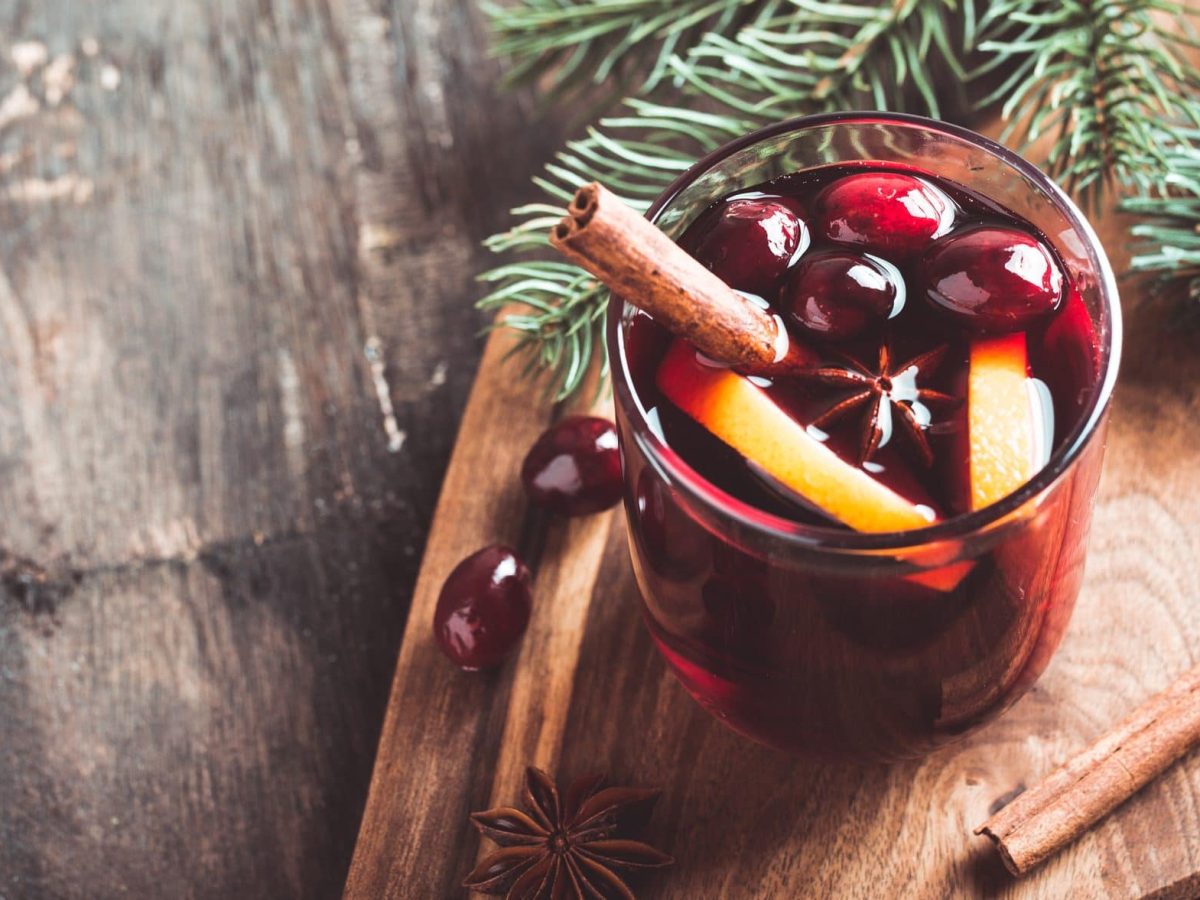 Unser Glühwein ohne Alkohol im Glas steht auf einem Holzbrett. Als Deko Gewürze und Tannenzweige.