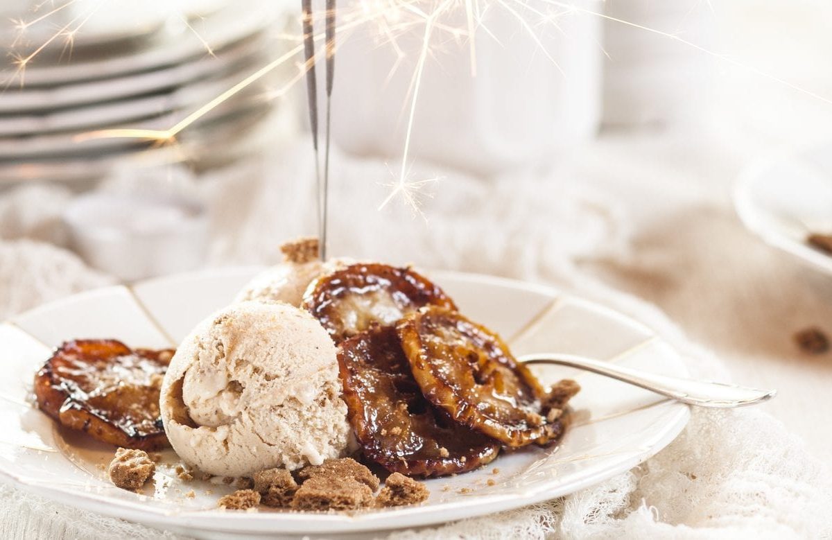 Unser Spekulatius-Eis weihnachtlich mit Wunderkerze auf weißen Tellern und Geschirr im Hintergrund in Szene gesetzt.