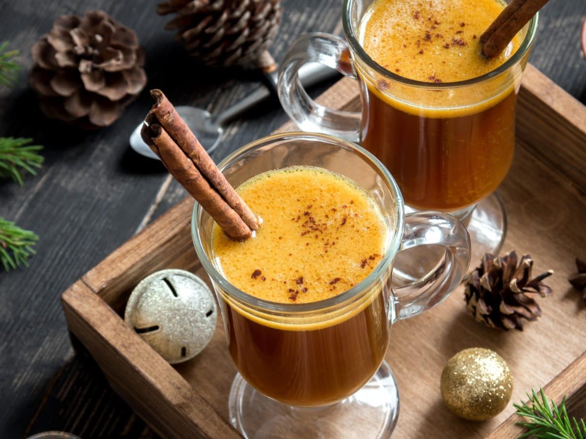 Der Hot Buttered Rum abgefüllt in zwei Trinkgläser. Rundherum weihnachtliche Deko.