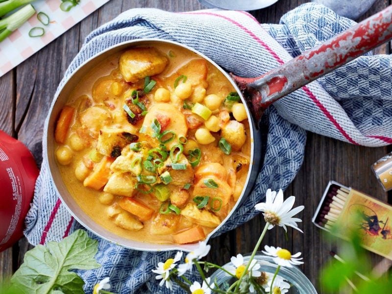 Unser Hähnchen-Kichererbsen-Topf angerichtet auf einem Tisch mit Blumen, Deko und Gewürzen.