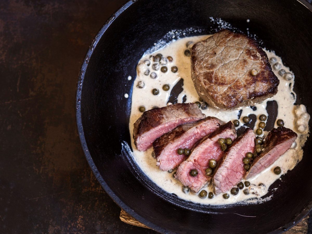 Pfanne mit Steak in Pfefferrahmsauce auf dunklem Untergrund