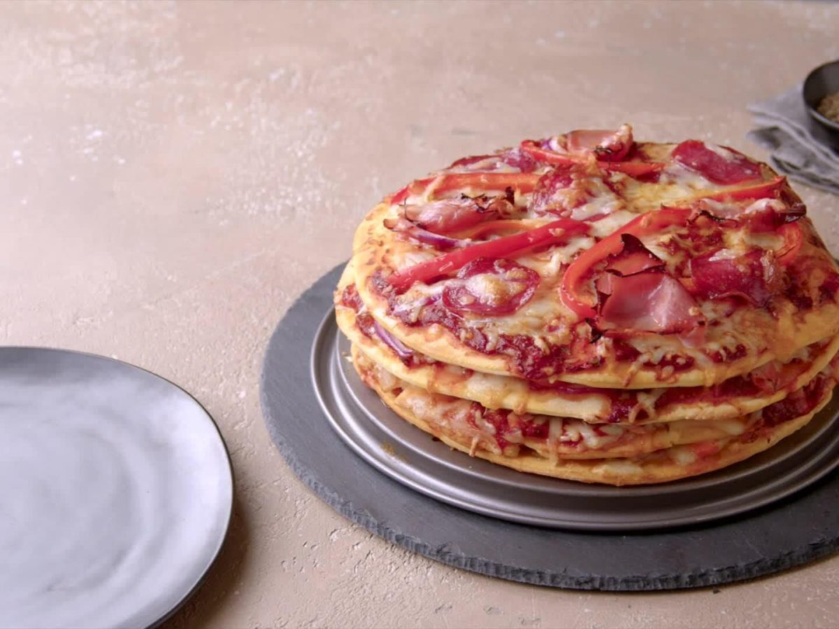 Pizzakuchen belegt mit Wurst und Paprika auf Schieferplatte.