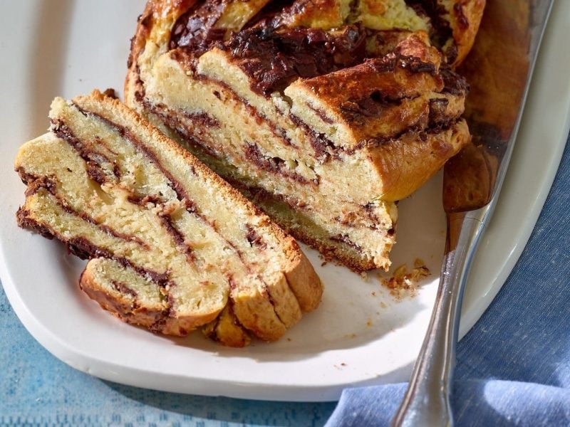 Der Schokoladen-Stollen liegt auf einer weißen Kuchenplatte. Ein Stück ist bereits abgeschnitten.