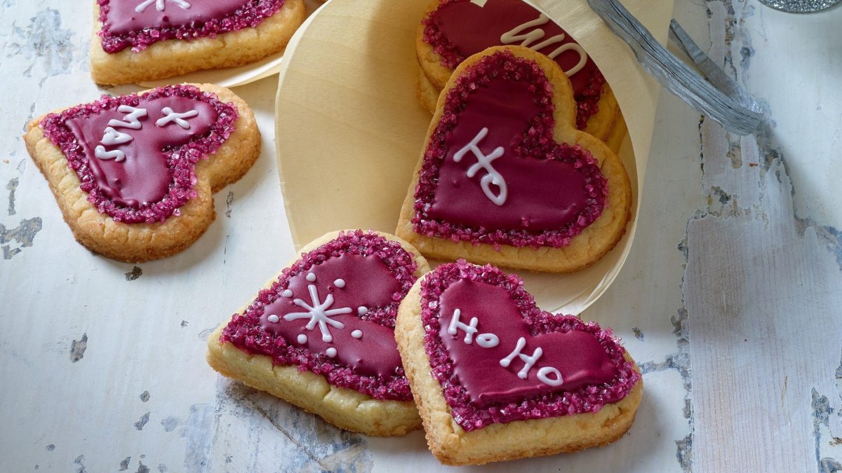 Weihnachtsherzen, Plätzchen in Herzform, mit roter Lebensmittelfarbe bemalt und mit weißer Farbe beschriftet.