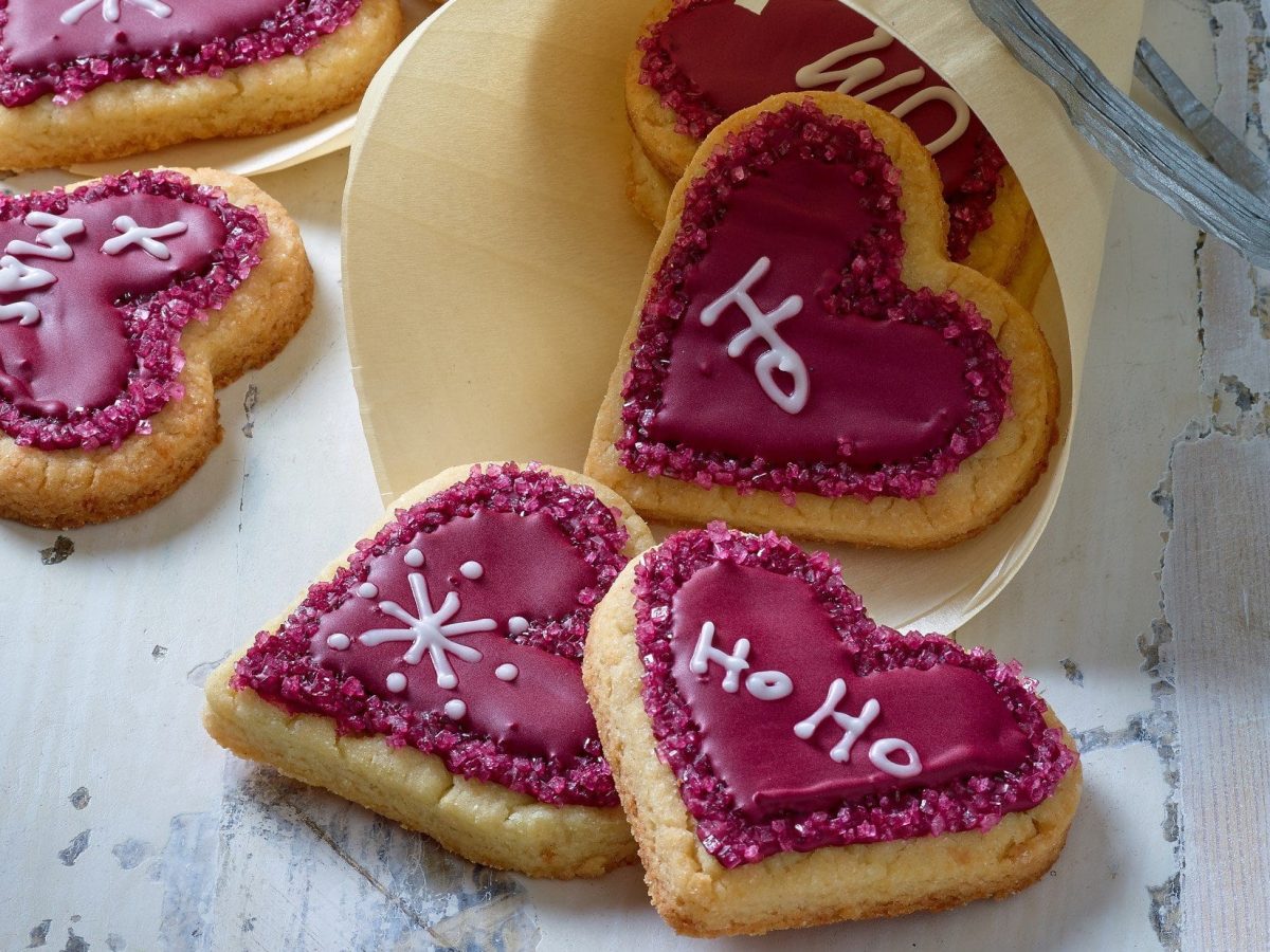 Weihnachtsherzen, Plätzchen in Herzform, mit roter Lebensmittelfarbe bemalt und mit weißer Farbe beschriftet.