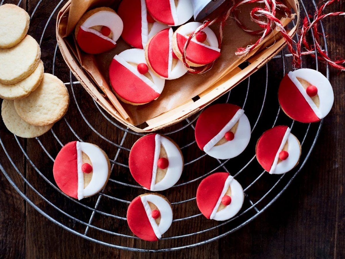 Mehrere Weihnachtsmann-Kekse liegen verteilt auf einem Gitter und in einem kleinen Korb auf einem dunelbraunen Tisch.