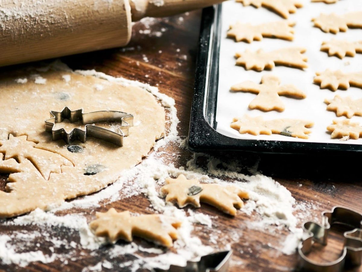 Ausgestochene Plätzchen mit weihnachtlichen Motiven auf hölzernem Untergrund.