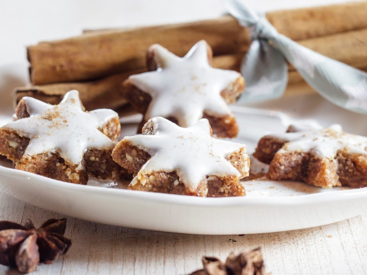 Zimtsterne mit Glasur auf weißem Teller umgeben von weihnachtlicher Dekoration.