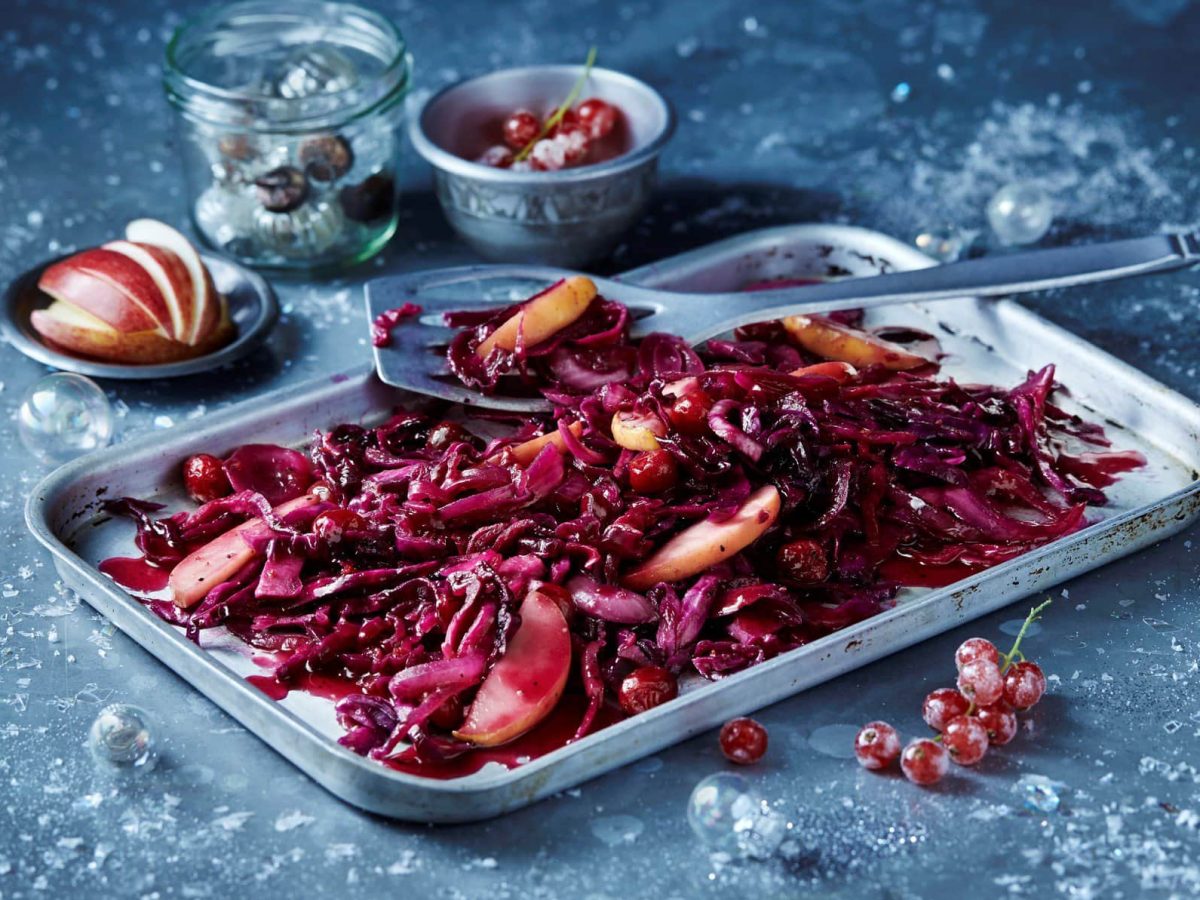 Ein Blech mit Apfel-Rotkohl auf vereistem Untergrund, daneben liegen gefrostete Johannisbeeren und einige weitere Zutaten.