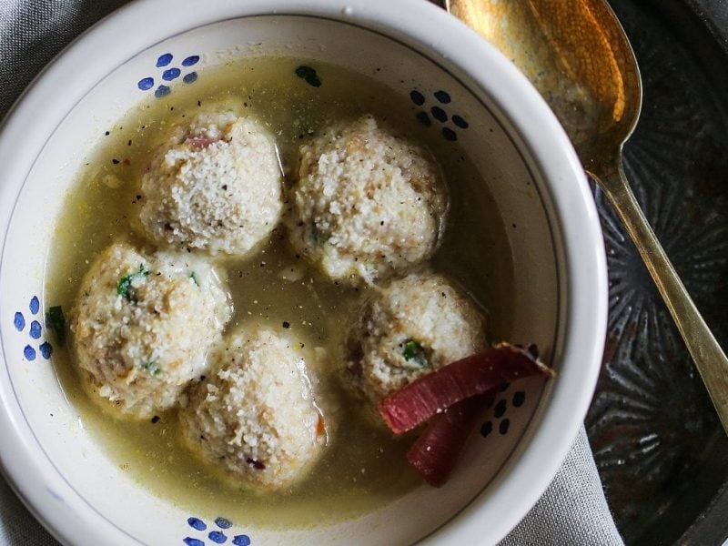 Unsere bayrischen Semmelknödel mit Speck schwimmen in einer Gemüsebrühe in einer Schale.