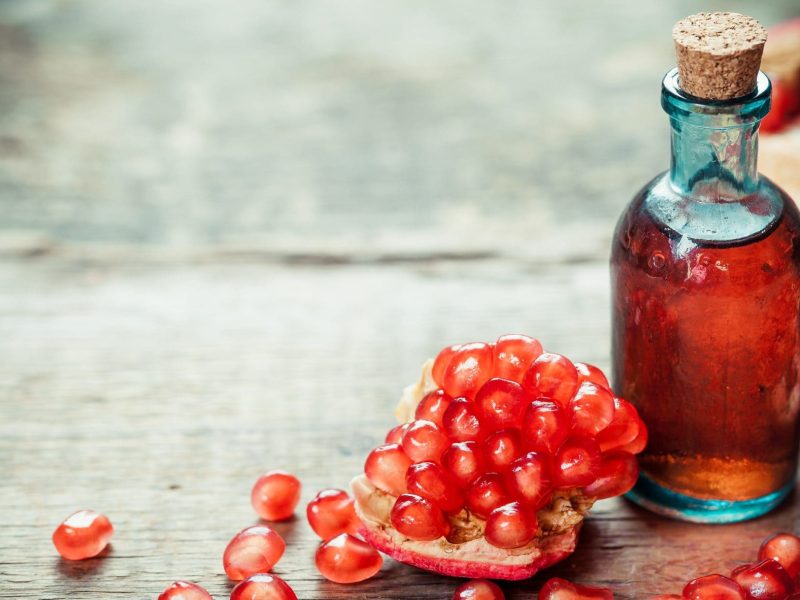 In einer Glasflasche ist eine rote Flüssigkeit. Es handelt sich um Granatapfel-Sirup. Daneben liegen Granatapfelkerne.