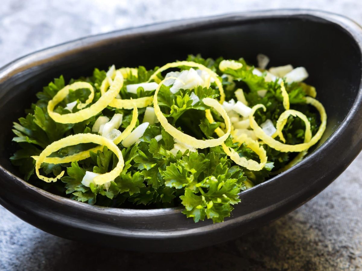 In einer ovaeln schwarzen Schale sind Petersilienblätter und Zitronenzesten als Gremolata.