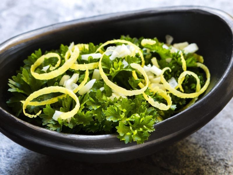 In einer ovaeln schwarzen Schale sind Petersilienblätter und Zitronenzesten als Gremolata.