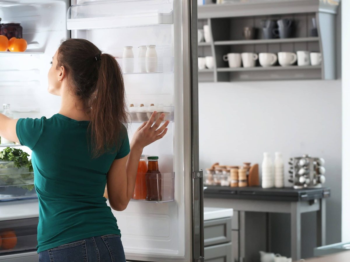 Wie lange ist gekochtes Essen im Kühlschrank haltbar? Frau am Kühlschrank mit Lebensmitteln und Gerichten