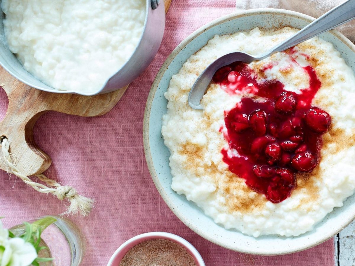 Unser Milchreis mit Kirschen angerichtet in einer Dessertschüssel auf einer rosa Tischdecke.