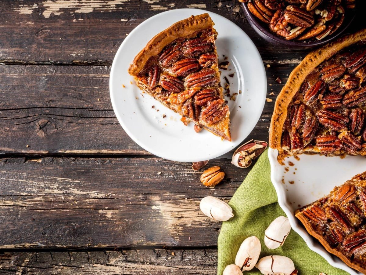 Ein angeschnittener Pecan Pie in einer Tarteform, daneben steht ein Teller mit einem Stück des Kuchens.