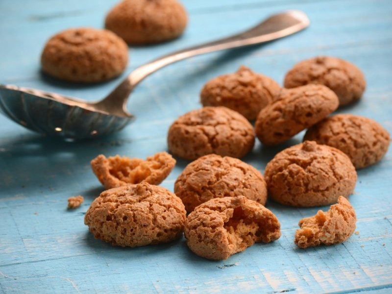 Auf blauem Holz liegen selbst gemachte Amaretti-Kekse und ein Löffel.