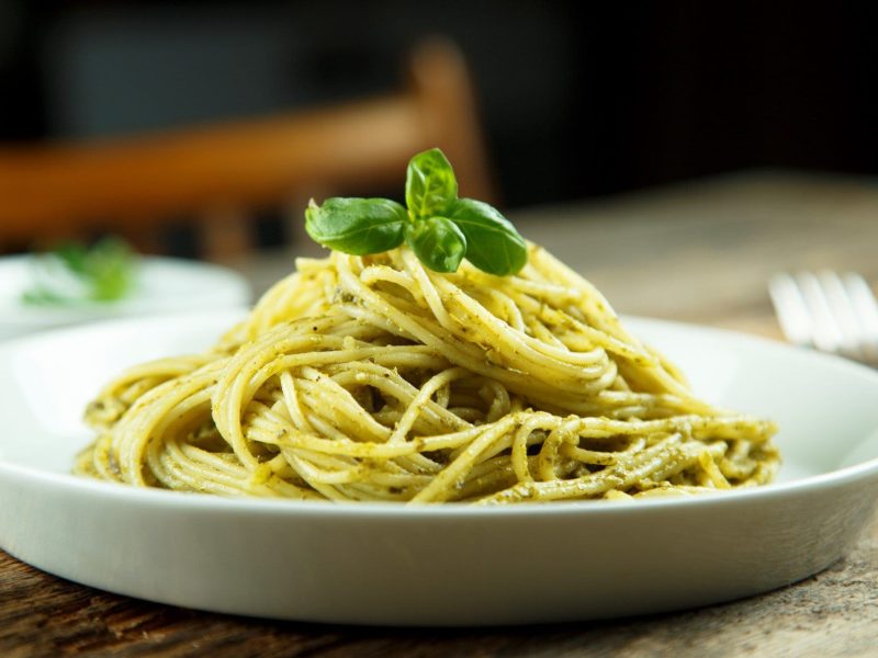 Ein Teller Spaghetti mit Gin-Soße, dekoriert mit Basilikum, steht auf einem Holztisch.