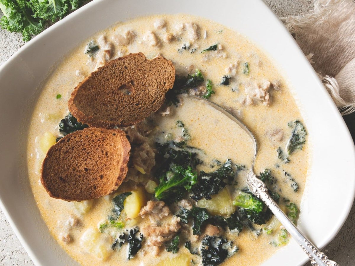 toskanische Kartoffelsuppe mit Grünkohl und Hackfleisch in einer wieißen Schüssel, garniert mit Brotscheiben