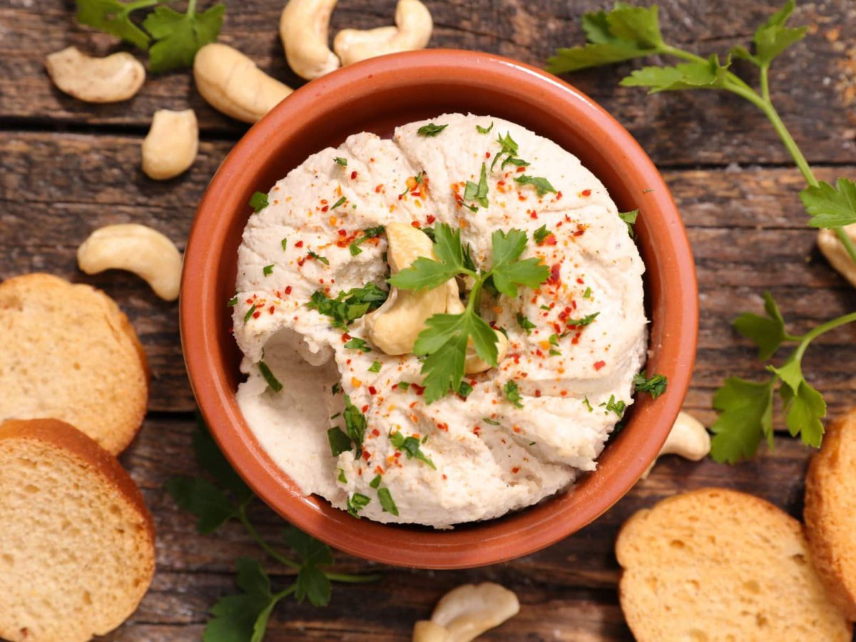 Eine Schale vegane Auberginencreme in der Draufsicht, drumherum liegen Zwiebackscheiben und Cashews.