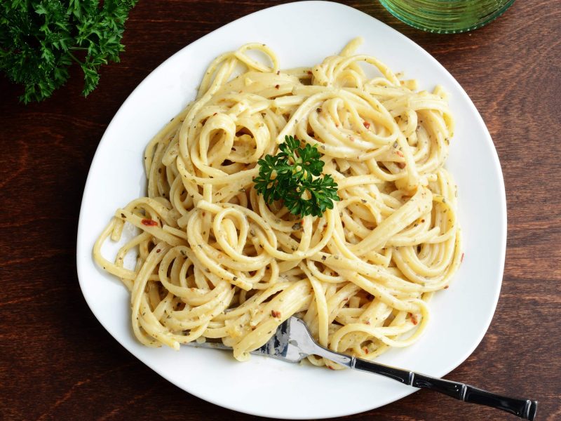 Auf einem Holztisch steht ein Teller in der Draufsicht, darauf vegane Spaghetti Carbonara mit Petersilie dekoriert.