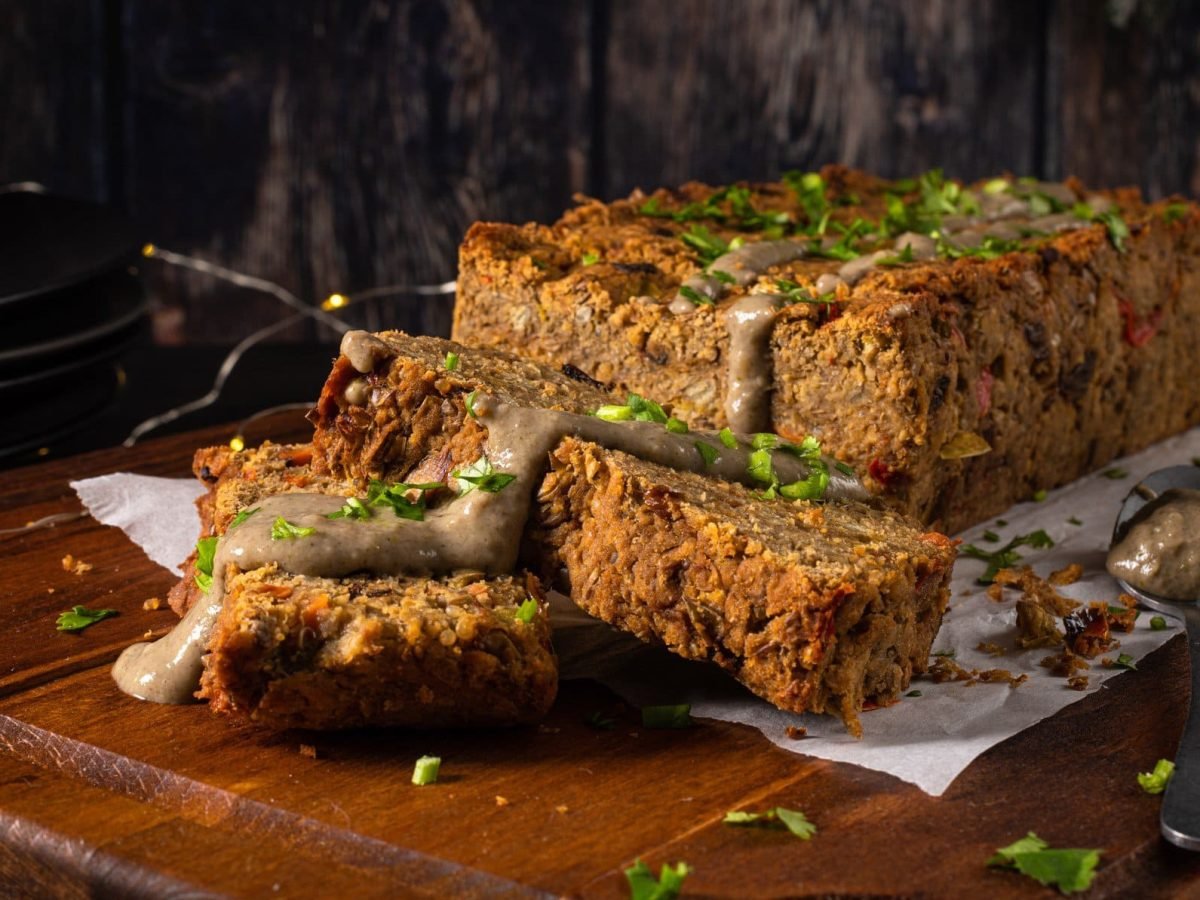 Auf einem Brett liegt ein angeschnittener veganer Nussbraten, bestreut mit Petersilie. Im Hintergrund ist eine Lichterkette erkennbar.