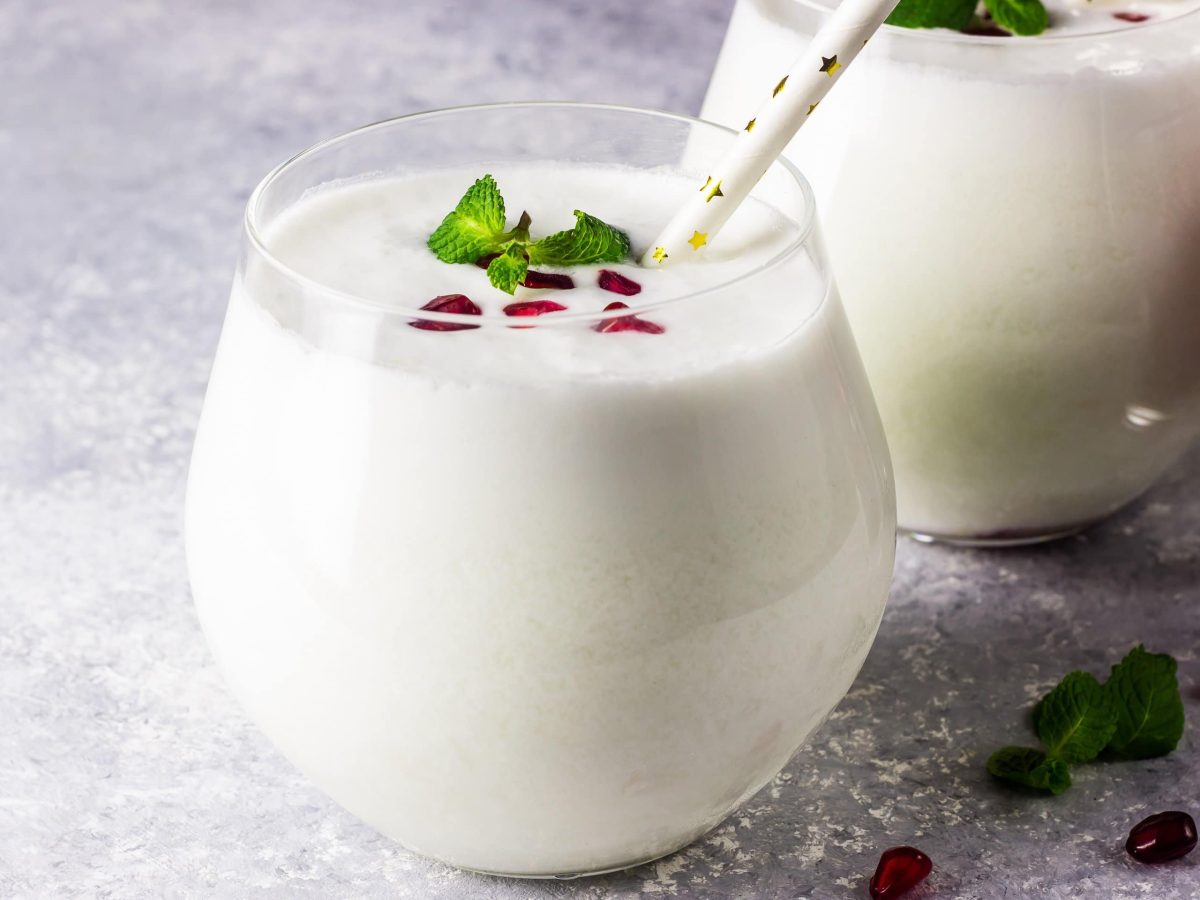 Zwei Gläser White Christmas Mojito dekoriert mit Granatapfelkernen und MInzblättern. Daneben steht ein Glas mit Granatapfelkernen.