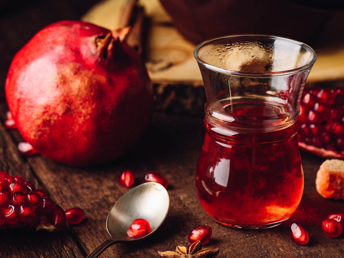 Euf einem Tisch steht ein Glas mit Granatapfeltee. Daneben liegt ein Granatapfel.