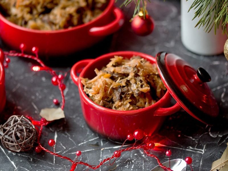 Topf mit Bigos umgeben von weihnachtlicher Dekoration auf dunklem Untergrund.