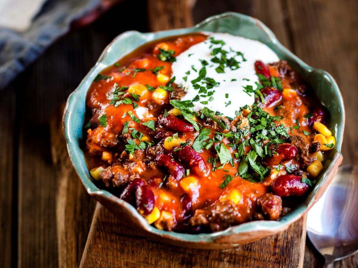 Chili con carne mit Hackfleisch, Bohnen und Mais, garniert mit Sour Cream und Koriander.