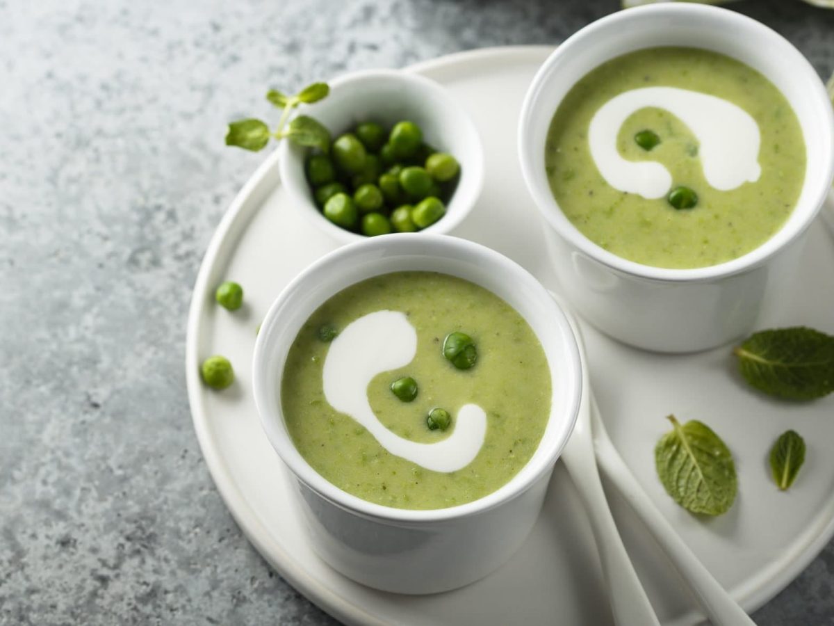 Unsere feine Erbsensuppe angerichtet in zwei Becherschalen, die auf einem weißen Teller Platz finden.