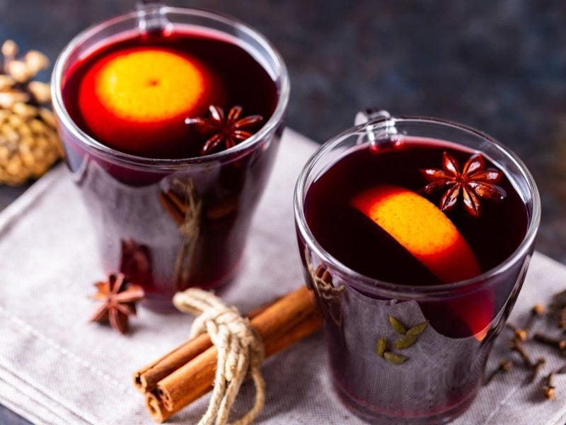 Zwei Tassen Glühwein mit Orangen und Gewürzen auf dunklem Untergrund