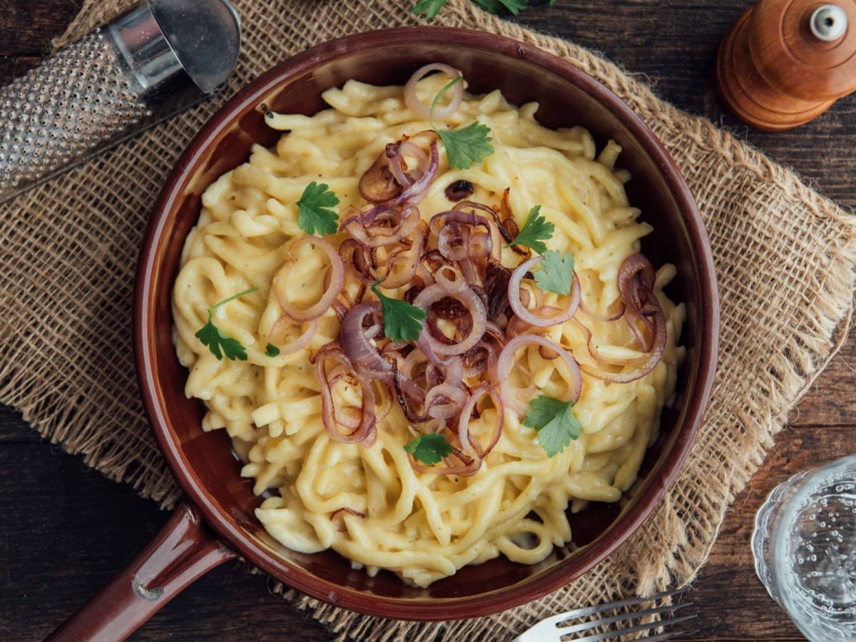 Pfanne mit Käsespätzle und Röstzwiebeln auf Holzuntergrund in rustikalem Ambiente.