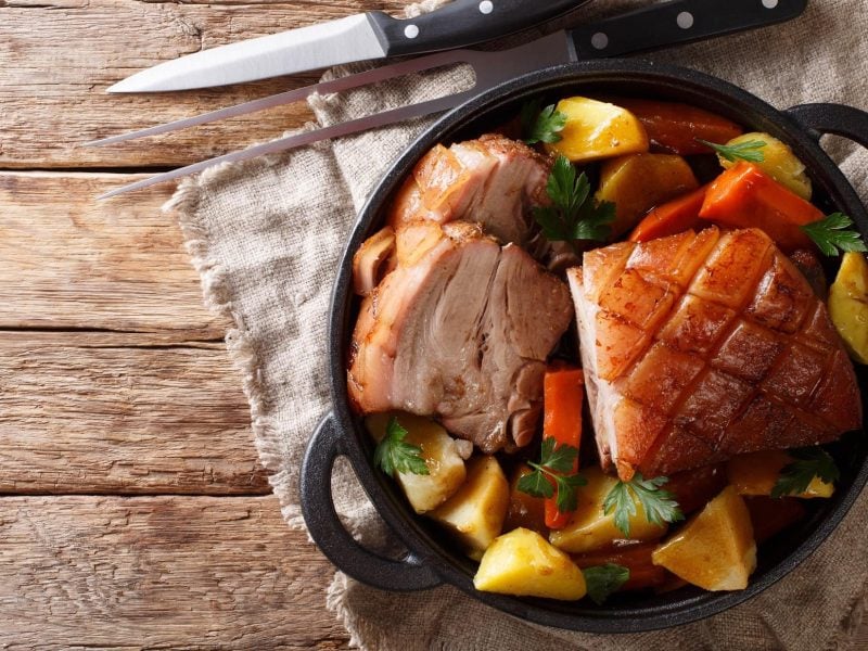 Krustenbraten in Gemüse auf Holzplatte.