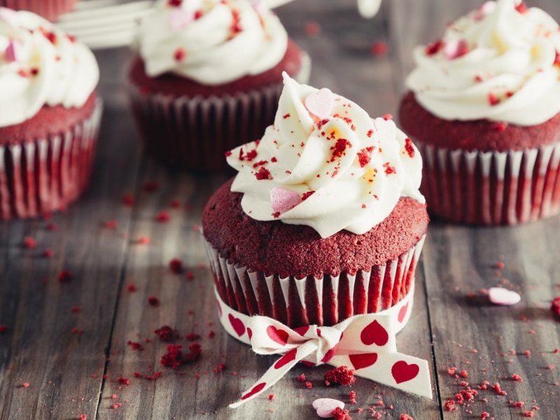 Red Velvet Cupcakes auf einem rustikalen Holztisch, dekoriert für den Valetinstag.