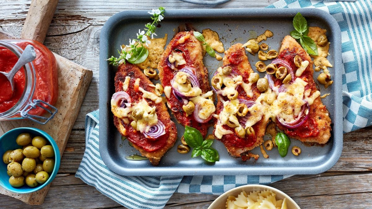 Ein Pizza-Schnitzel, mit Käse und Tomatensauce überbacken, auf einem Backblech serviert.