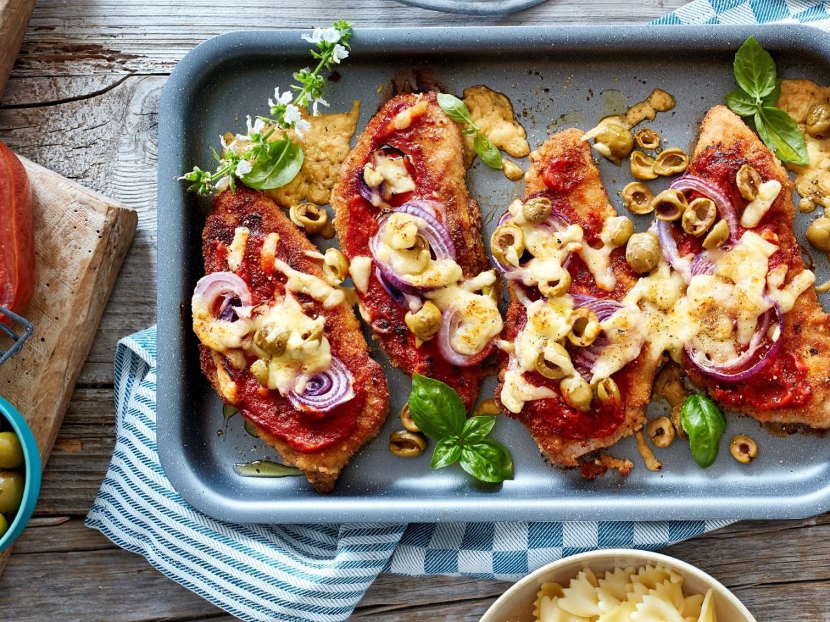 Ein Pizza-Schnitzel, mit Käse und Tomatensauce überbacken, auf einem Backblech serviert.