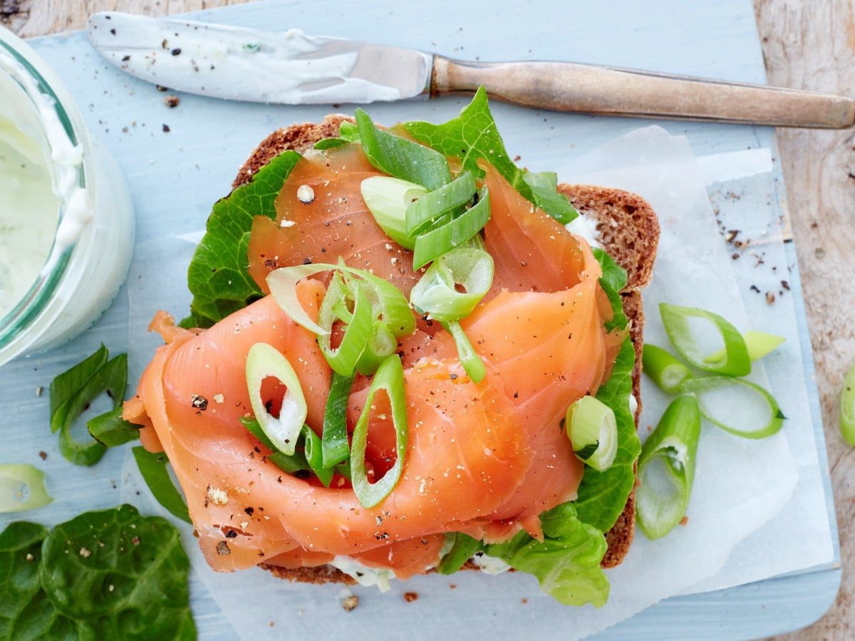 Vollkorn-Sandwich mit Lachs auf Holzbrett.