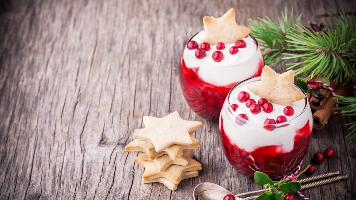 Dessertgläser gefüllt mit Granatapfel und weißer Schokocreme auf hölzernem Untergrund