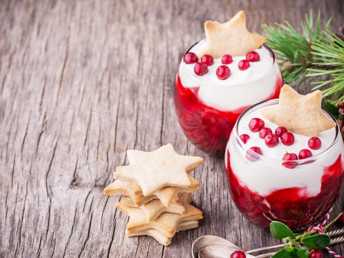 Dessertgläser gefüllt mit Granatapfel und weißer Schokocreme auf hölzernem Untergrund